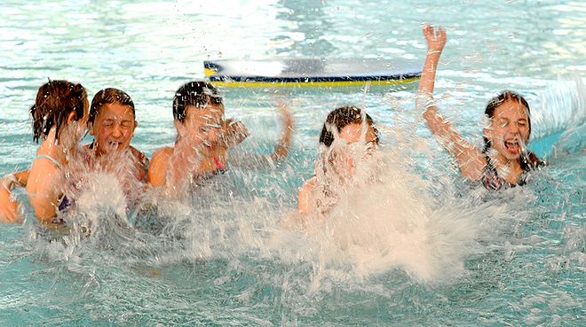 Eine Gruppe Kinder im Wasser, im Vordergrund spritzt viel Wasser nach oben, der Hintergrund ist unscharf. 