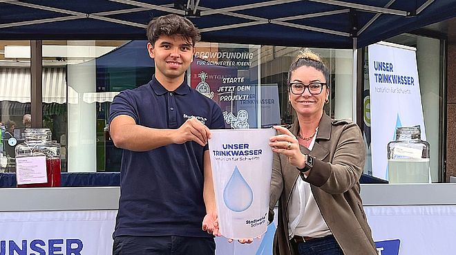 Zwei MItarbeiter der Stadtwerke Schwerte halten symbolisch einen großen Trinkbecher in die Kamera