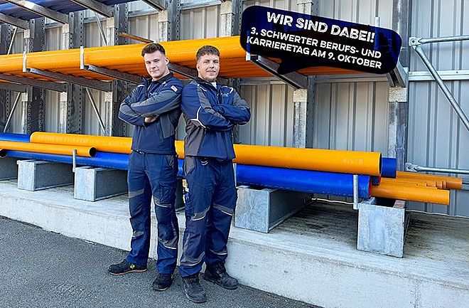 Zwei Auszubildende der Stadtwerke Schwerte in Arbeitskleidung stehen Rücken an Rücken vor einem Regal mit gelben und blauen Rohren. Daneben eine Sprechblase mit dem Hinweis: ‚Wir sind dabei! 3. Schwerter Berufs- und Karrieretag am 9. Oktober‘.