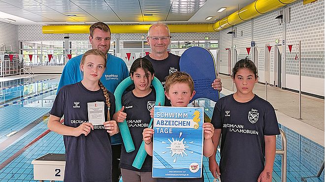 Kinder und zwei Männer mit einem Plakat im Stadtbad Schwerte