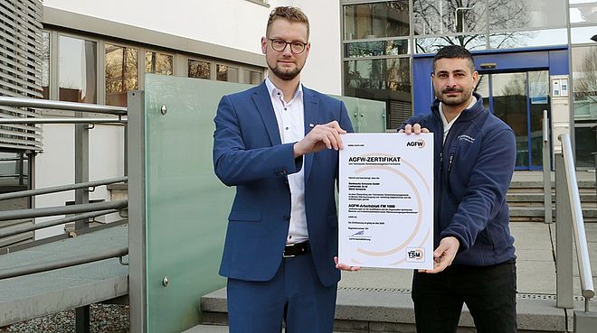 Dr. Jens Priebe und Ergün Yildirim halten vor dem Gebäude der Stadtwerke Schwerte die Urkunde zur TSM-Zertifizierung hoch