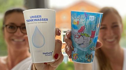 Schwerter Wasser auf dem Pannekaukenfest Zwei Mitarbeiterinnen der Stadtwerke Schwerte halten die Mehrwegbecher für das Wasser auf dem Pannekaukenfest hoch.