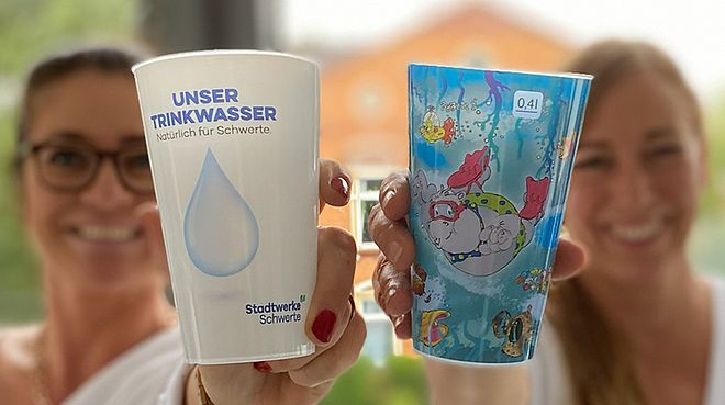 Zwei Mitarbeiterinnen der Stadtwerke Schwerte halten die Mehrwegbecher für das Wasser auf dem Pannekaukenfest hoch.