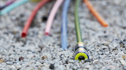 Auf dem Bild sieht man mehrere bunte Glasfaserkabel auf dem Boden liegen. Es deutet alles auf eine Baustelle hin.