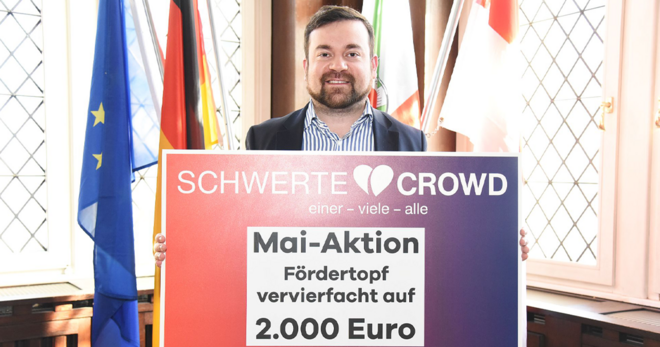 Auf dem Bild sieht man den Bürgermeister von Schwerte, Dimitrios Axourgos. Er hält ein Schild der Schwerte Crowd zur Mai-Aktion in der Hand.