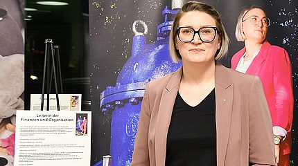 Eine Mitarbeiterin der Stadtwerke Schwerte steht vor einer großformatigen Fotografie und einem Schild mit Erklärungen zu ihrem beruflichen Werdegang.