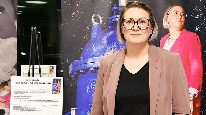 Eine Mitarbeiterin der Stadtwerke Schwerte steht vor einer großformatigen Fotografie und einem Schild mit Erklärungen zu ihrem beruflichen Werdegang.