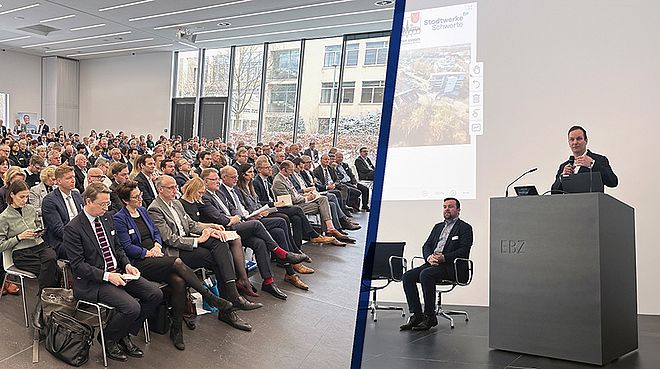 Großer Saal mit zahlreichen sitzenden Teilnehmern bei einer Präsentation, Sprecher Sebastian Kirchmann steht am Rednerpult mit 'EBZ' Schriftzug, zweite Person, Dimitri Axourgo, sitzt auf Stuhl neben Bühne