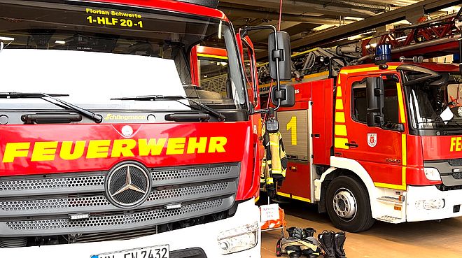 Zwei rote Feuerwehrwagen der Feuerwehr Schwerte stehen geparkt in einer Feuerwehrgarage.