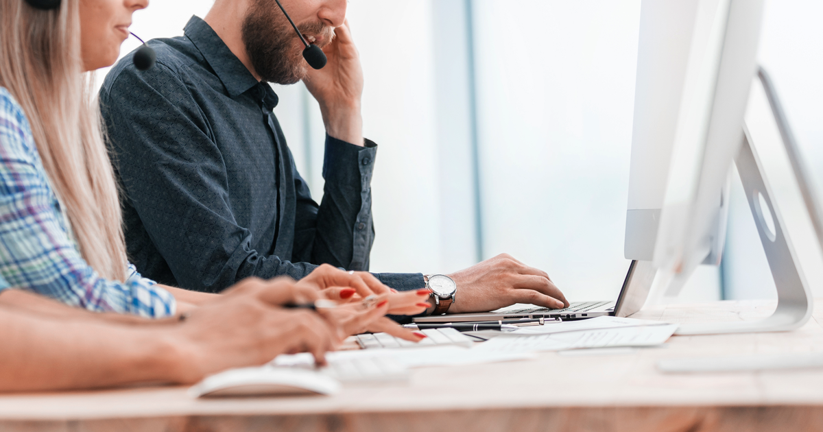 Zwei Menschen sitzen mit Headset vor jeweils einem Computer und führen telefonisch eine Umfrage durch.