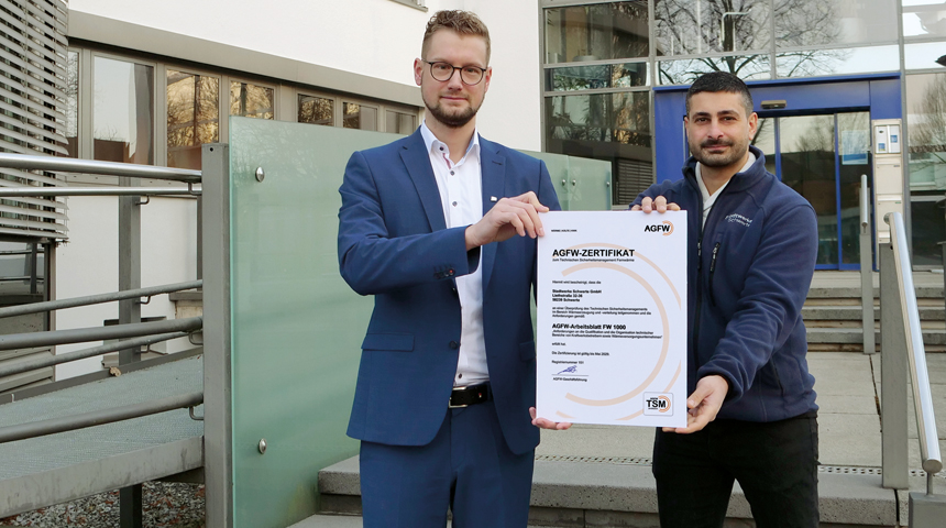 Dr. Jens Priebe und Ergün Yildirim halten vor dem Gebäude der Stadtwerke Schwerte die Urkunde zur TSM-Zertifizierung hoch
