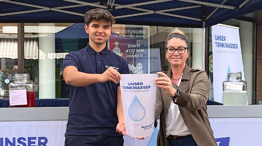 Zwei MItarbeiter der Stadtwerke Schwerte halten symbolisch einen großen Trinkbecher in die Kamera