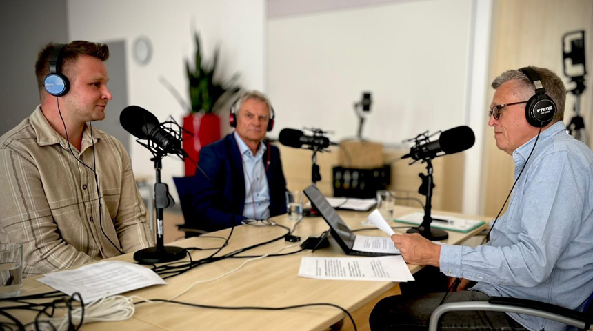 Drei Männer sitzen mit Kopfhörern und Mikrofonen in einem Studio und sprechen miteinander. Vor ihnen liegen Notizen und ein Laptop – es handelt sich um eine Podcast-Aufnahme.