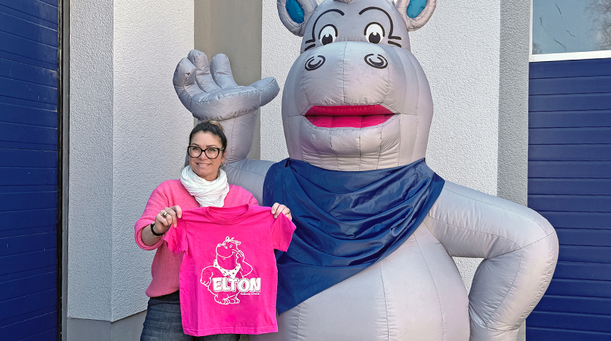 Eine Mitarbeiterin der Stadtwerke Schwerte stehet neben einem großen aufblasbaren Nilpferd und hält ein Pinkes Kinder-T-Shirt mit Aufdruck nach oben. 