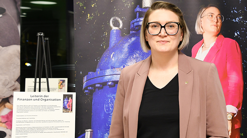 Eine Mitarbeiterin der Stadtwerke Schwerte steht vor einer großformatigen Fotografie und einem Schild mit Erklärungen zu ihrem beruflichen Werdegang.