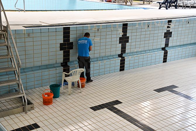 Ein Mitarbeiter aus dem Stadtbad Schwerte steht im leeren Schwimmerbecken und nimmt Reparaturarbeiten am Fliesenspiegel vor.