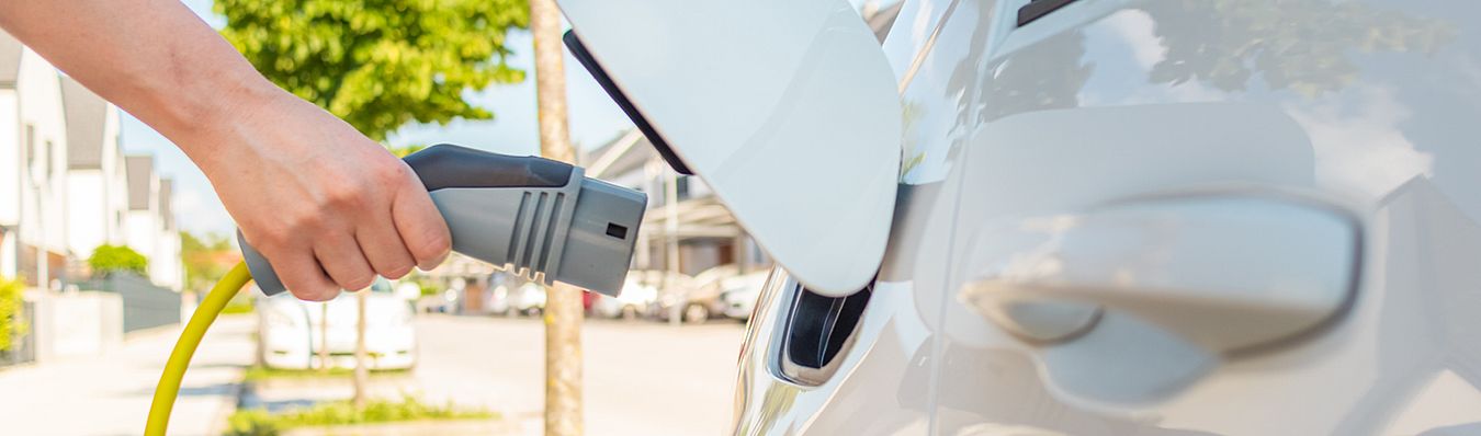 Eine Hand steckt ein Ladekabel in die Ladeöffnung an einem Elektrofahrzeug.