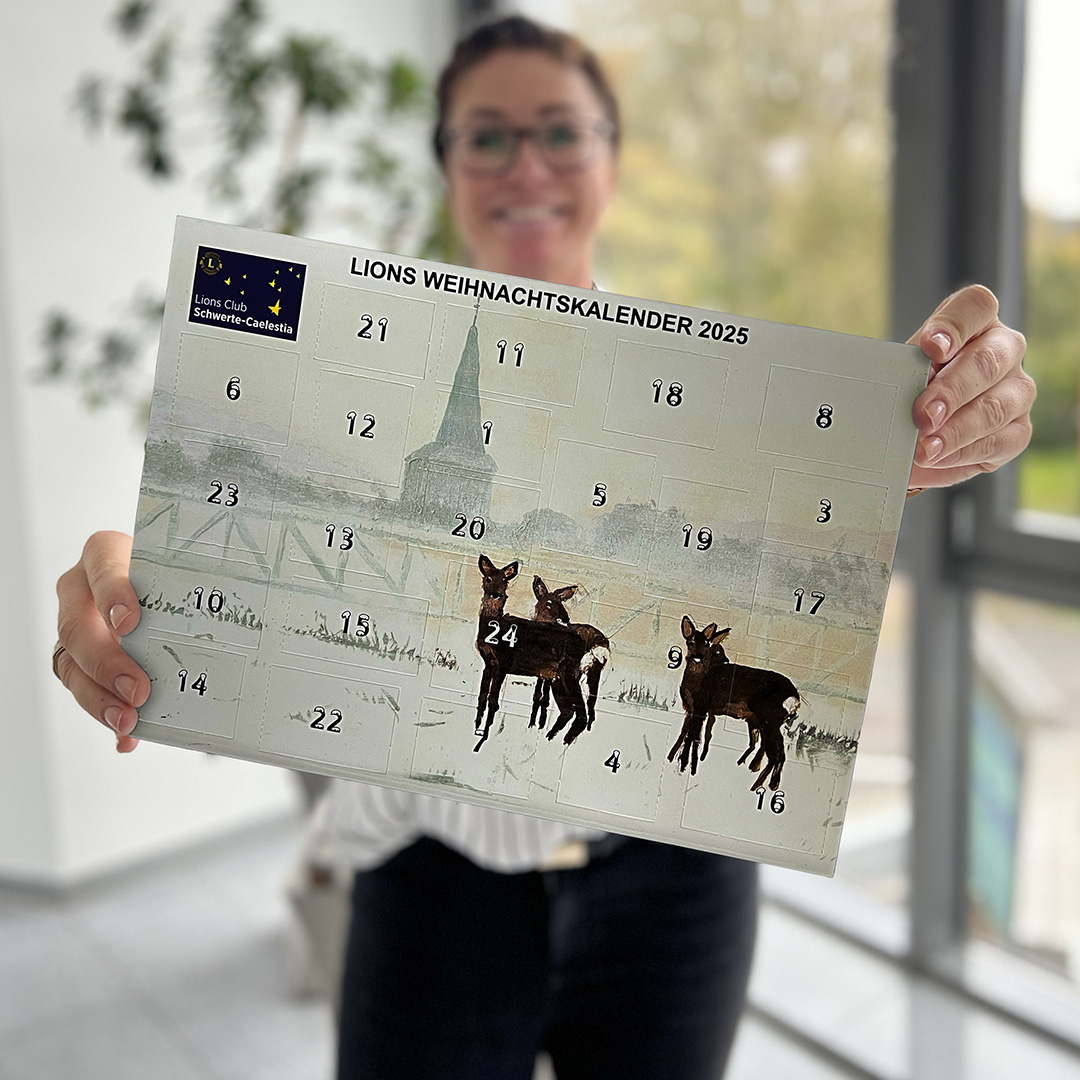 Eine Frau zeigt lächelnd einen Adventskalender in die Kamera, der Hintergrund ist unscharf.