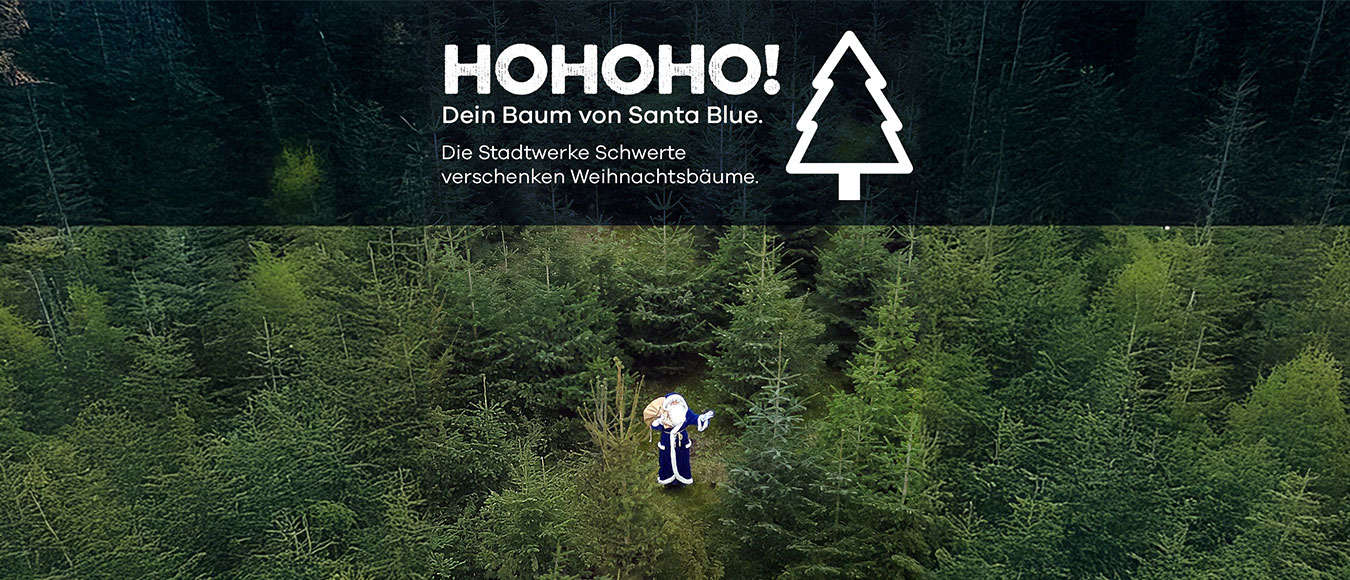 Vogelperspektive auf eine Person im blauen Weihnachtsmannkostüm, die im Tannenwald steht und in die Kamera winkt. Oben ist der Schriftzug ‚HoHoHo! Dein Baum von Santa Blue. Die Stadtwerke Schwerte verschenken Weihnachtsbäume.‘ zu sehen.